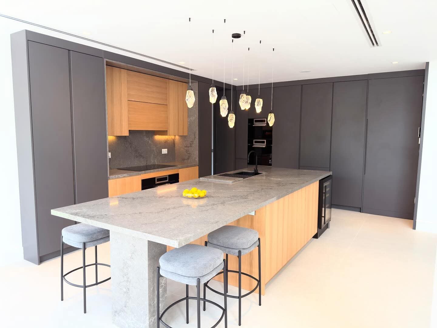 Completed kitchen renovation in Dubai with graphite and timber cabinetry, marble-topped island and pendant lighting